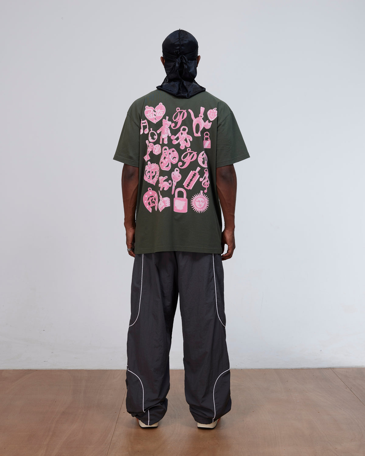 Back view of model wearing the Patta Charm T-Shirt in Climbing Ivy green with pink graphics on the back.